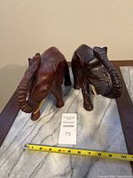 Two carved wooden elephants on marble and wooden surface with measuring tape showing approximate length