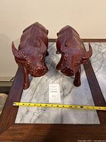Frontal view of two carved wooden water buffalo on a marble and wood table showing size and scale with tape measure.
