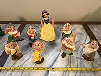 All eight figurines arranged on marble-patterned tabletop with measuring tape showing scale