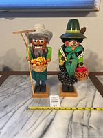 Front view of both vintage nutcrackers, showing overall condition and approximate size with measuring tape and auction card.