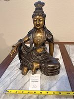 Front view of the bronze Guan Yin statue with measuring tape showing width approximately 8 inches and height around 10 inches.