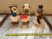 Front view of three wooden figures including Grandma and Grandpa smoker/music boxes and the Shepherd smoker figurine with sheep on gray marble surface with measuring tape showing approx 9 inches height.