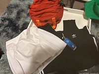 Orange Lululemon bag lying on a white surface beside black Adidas dress and white Nike skort