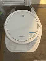 Photo of the white Bissell SpinWave robot vacuum placed on its charging dock on wooden flooring.