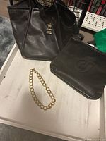 Photo showing the Anne Klein large black leather handbag, Charles Jourdan smaller black leather shoulder bag, and gold-tone chunky chain necklace all on a white surface