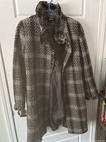Front view of black and grey checkered DKNY wool trench coat hanging on blue hanger showing collar, buttons, and length.