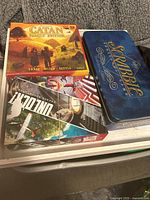 Three family board games together: Catan Family Edition, Scrabble Original tin, and Unlock! game with colorful artwork