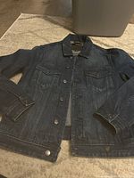 Front view of Guess Dillon denim jacket laid flat on carpet, showing button front, collar, chest pockets, and sleeves.