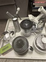 Photo showing multiple kitchen gadgets on white surface including Bialetti espresso maker, Big Boss juicer, KitchenAid meat grinder attachment, whipped cream dispenser, and yogurt maker.