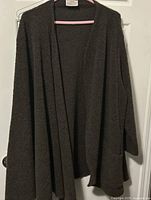 Front view of dark brown asymmetrical cape with single sleeve hanging on a hanger