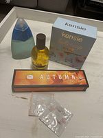 Photo of Kensie Buttercup Babe boxed perfume bottle, blue liquid perfume bottle, Autumn Essential Oils box, and two foil sample sachets