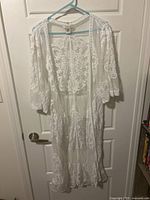 Full view of white lace kimono hanging on a door showing its length and front open style.