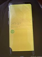 Samsung Galaxy S8 smartphone powered on showing 'Let's go!' setup screen with cracked screen and yellow discoloration.