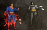 Superman and Batman McFarlane figures side by side showing costumes, capes, and accessories.