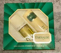 Front view of the original green and white Emeraude gift box showing spray cologne and talc powder tubes inside.