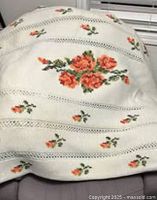 Full view of the cream throw blanket highlighting the cross-stitched rose floral motif arranged in horizontal bands separated by openwork strips.