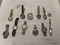 Overview of 12 watches of mixed styles, materials, and colors, arranged on a flat surface.
