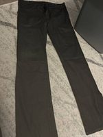 Full length view of black William Rast jeans laid flat on carpet, showing straight leg cut and matte black finish.