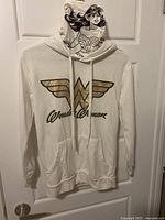 Full front view of white Wonder Woman hoodie with hood up showing printed Wonder Woman character and gold logo on front