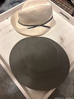 Two wool hats pictured on a white tray, one cream/off-white and one black.