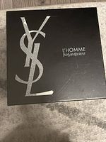 Front view of the black gift box with large silver YSL logo and L'Homme Yves Saint Laurent text.