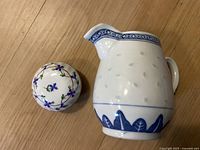 Porcelain tea kettle with blue decorative border and base detail alongside a spherical trinket box with blue floral design on wooden floor.