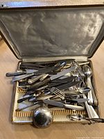 Silverware pieces displayed inside open storage case showing mixed knives, forks, spoons and serving utensils.