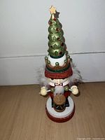 Front view of a Christmas tree-themed nutcracker, showing the green glittered tree hat with red ornaments, white beard, and drum at the base.