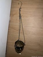 Full view of hanging silver cup holder showing chain and hook, placed on wood floor.