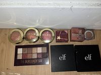 Top view of assorted makeup including Milani blushes, small eyeshadow compacts, and e.l.f. black compacts