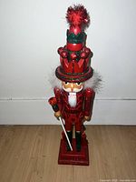 Front view of tall red sparkling nutcracker on wooden floor against white wall.