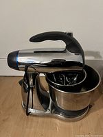 Front-side view of mixer showing chrome body, black handle and stainless steel bowl mounted on base