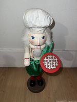 Front view of wooden nutcracker figurine dressed as a chef holding a pizza