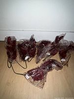 Eight red glitter-coated branches wrapped in plastic with metal stems on wooden floor