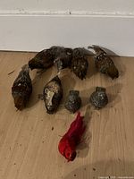 Top view of six brown silk bird ornaments, three silver/metal decorative elements and one bright red silk bird ornament arranged on wooden floor.