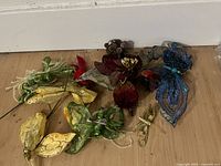 Silk floral and leaf decorations with glitter detail in red, blue, green, yellow hues arranged on a floor.