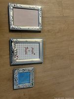 Set of 3 silver picture frames laid out flat on wood floor showing scale and details