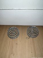 Two silver glitter spiral spherical ornaments seen side by side on a wooden floor against white baseboard.