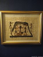 Framed Egyptian papyrus painting depicting Nut goddess arched over four human figures, painted with traditional Egyptian colors on papyrus, in a gold frame.