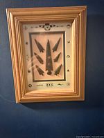 Framed display of seven Aboriginal arrowheads with indigenous motifs background and wooden frame
