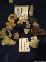 Overview of various rough mineral and rock specimens arranged on dark fabric along with a mineral sample set and identification card