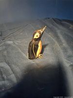 Side angle of the small carved horn bird figurine on a dark fabric background showing detailed carving, natural horn color variations, and glossy finish.