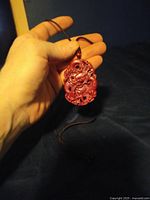 Hand holding the red cinnabar lacquered pendant showing detailed carving of dragon and floral motifs attached to a brown cord.