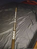 Full length view of the black Hespeler 2000 hockey stick on a bed with its branding visible
