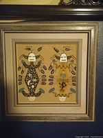 Framed sand painting featuring two figures in native attire with geometric designs.