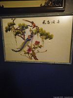 Photo of framed Japanese silk artwork with birds, flowers, and Japanese script, showing entire piece and frame.