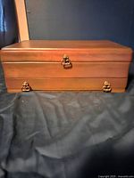 Exterior view of a closed wooden jewelry box with metal clasps and feet, rectangular shape with warm brown finish.