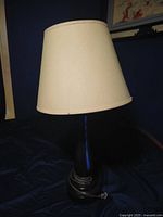 Full view of the lamp with beige tapered fabric shade and dark brown base on a dark surface.