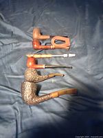 Photo showing five different smoking pipes laid out on a dark fabric background.