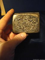 Front exterior of the metal cigarette case showing an embossed dragon design on the surface.